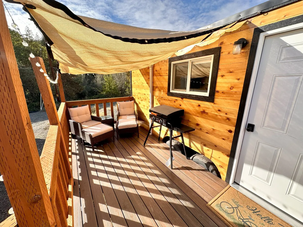 A comfortable outdoor seating area is arranged on a wooden deck, complete with a grill and shaded by a canopy. The setup encourages socializing, relaxation, and outdoor dining while maintaining a sense of comfort and style. The scene conveys an inviting mood, ideal for group gatherings or quiet moments alike.
