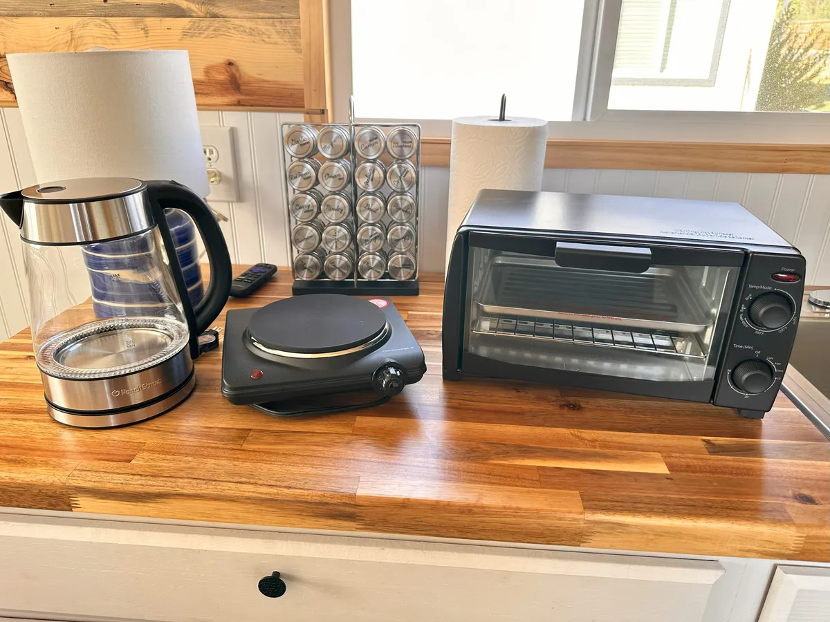 A functional kitchen vignette focusing on an electric kettle, hot plate, toaster oven, and paper towel holder arranged on a tidy counter. The setup emphasizes practical, essential appliances for making coffee or preparing small meals.